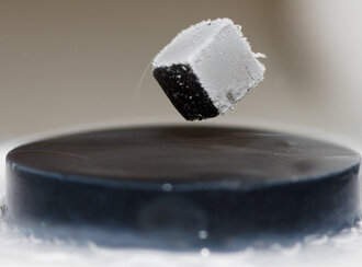 A frost-covered magnet cube floats above a black superconductor disc.