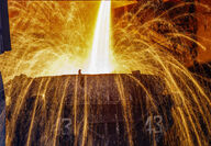 Showers of sparks arc out of a vat being filled with molten steel.