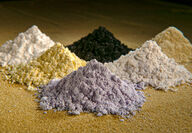 Piles of grey, yellow, white, and black rare earth oxide powders.