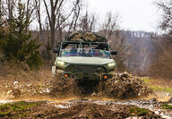 U.S. military version of the Hummer EV charging through mud on an autumn day.