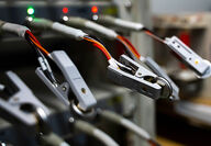 Coin battery cells being held by clamps connected to a diagnostic machine.