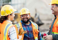 A woman and two men smiling in hard hats.