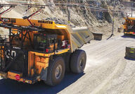 Two Komatsu mining trucks being assisted uphill by overhead trolley assist.