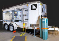 An enclosed trailer with open doors revealing TruScan controls and feed area.