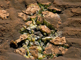 Greenish yellow crystals intermingled with fractured, red-stained rock.
